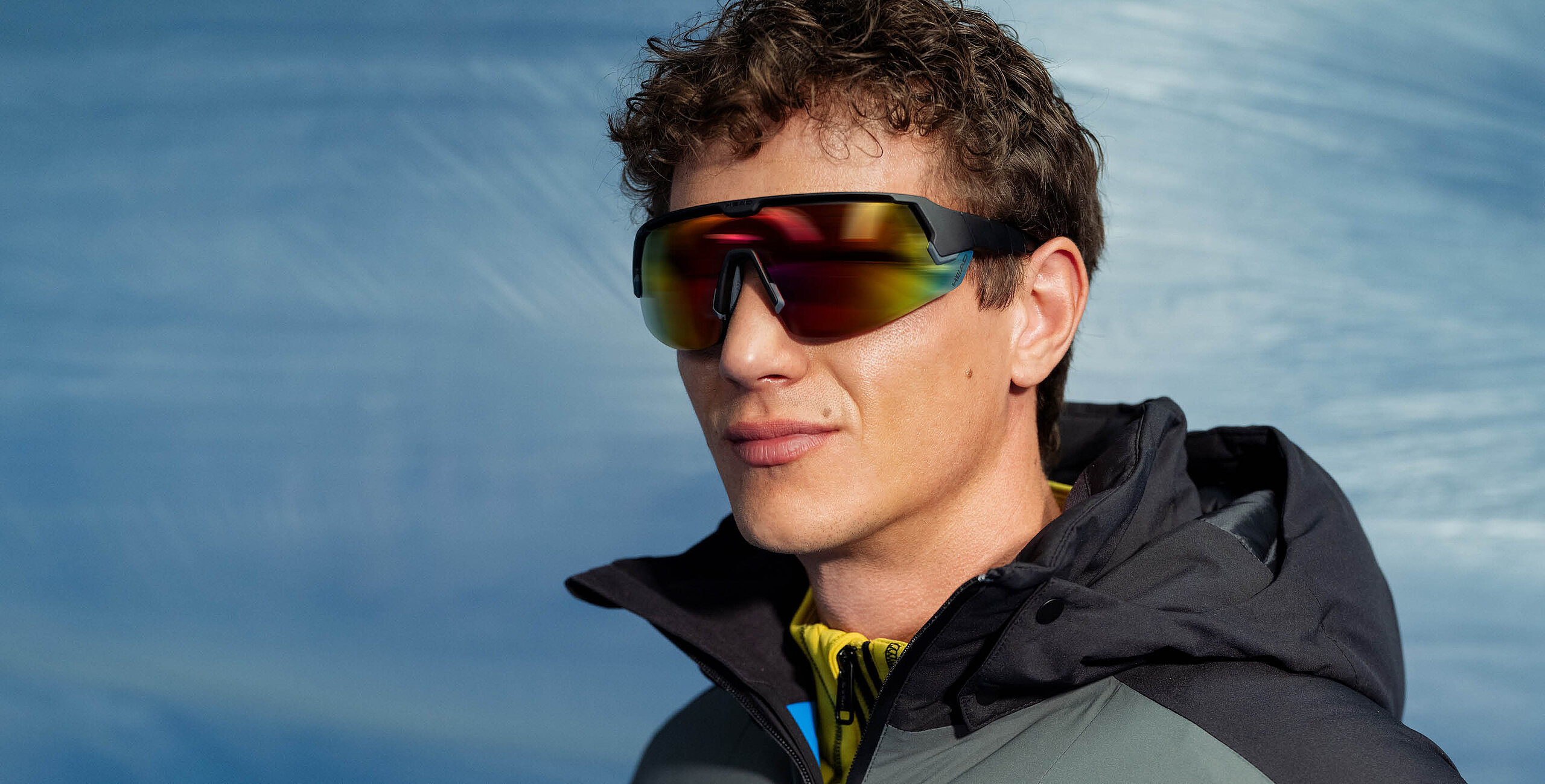 Man wearing mirrored shield sunglasses with HEAD logo and a dark winter jacket.